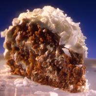 A slice of Marscapone Cake topped with coconut flakes placed on a thin gray square plate